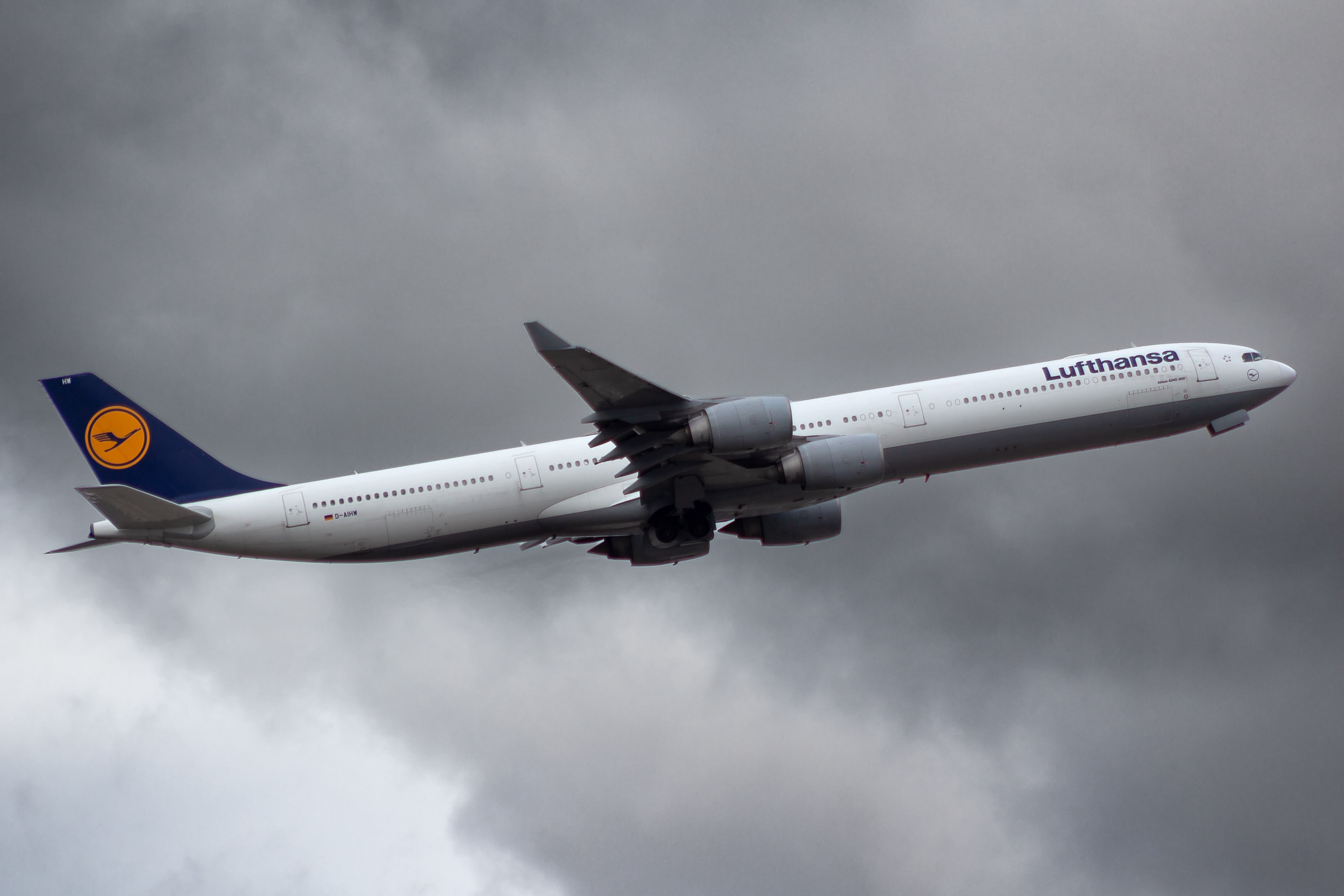 Lufthansa A340-600 D-AIHW im Steigflug vor dunklen Wolken